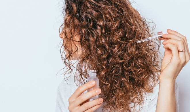 Woman with curly hair holding a hair serum up to her scalp