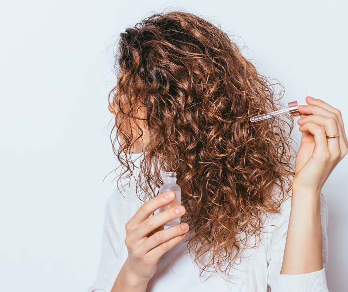 Woman with curly hair holding a hair serum up to her scalp